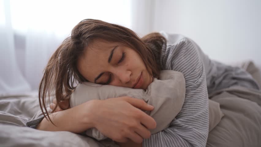 Young woman lies alone on bed at home, cold and sick. illness, cold, virus, doctor's call at home, consultation with a doctor by phone | Shutterstock HD Video #1099514065