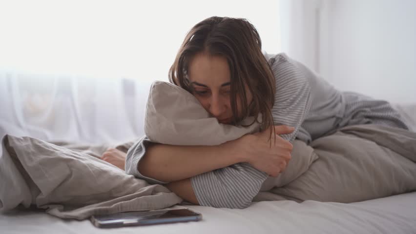 Young woman lies alone on bed at home, cold and sick. illness, cold, virus, doctor's call at home, consultation with a doctor by phone | Shutterstock HD Video #1099514067