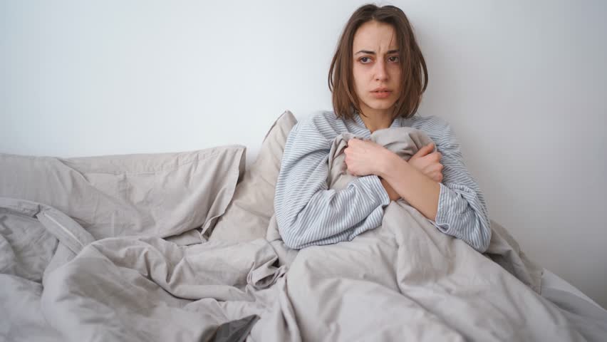 Young woman lies alone on bed at home, cold and sick. illness, cold, virus, doctor's call at home, consultation with a doctor by phone | Shutterstock HD Video #1099514077