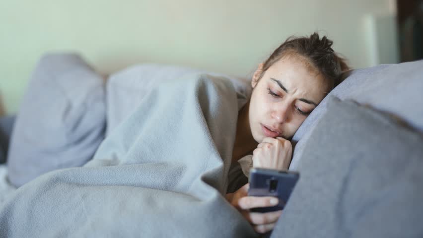 Young woman lies alone on bed at home, cold and sick. illness, cold, virus, doctor's call at home, consultation with a doctor by phone | Shutterstock HD Video #1099514079