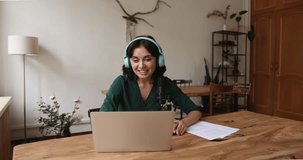 Positive Asian blogger woman wearing big wireless headphones, speaking at laptop and sound studio microphone, making video call, shooting, recording podcast, giving workshop, webinar