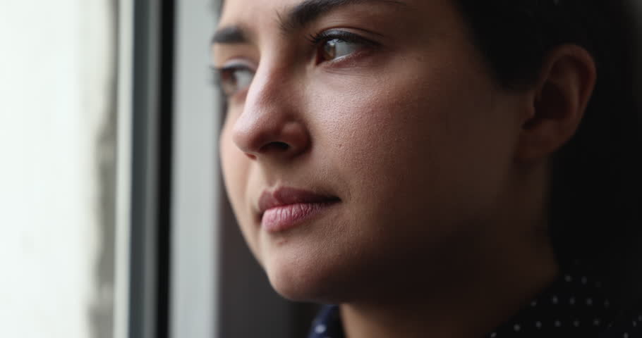 Face close up of thoughtful concerned pretty young Indian woman looking out of window deep in serious thoughts, thinking over problems, making decision, feeling worried, depressed Royalty-Free Stock Footage #1099514541