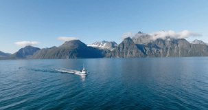 Fishing boat sailing in Lyngen fjord with Scandinavian Alps in background, Norway. Aerial backward and sky for copy space