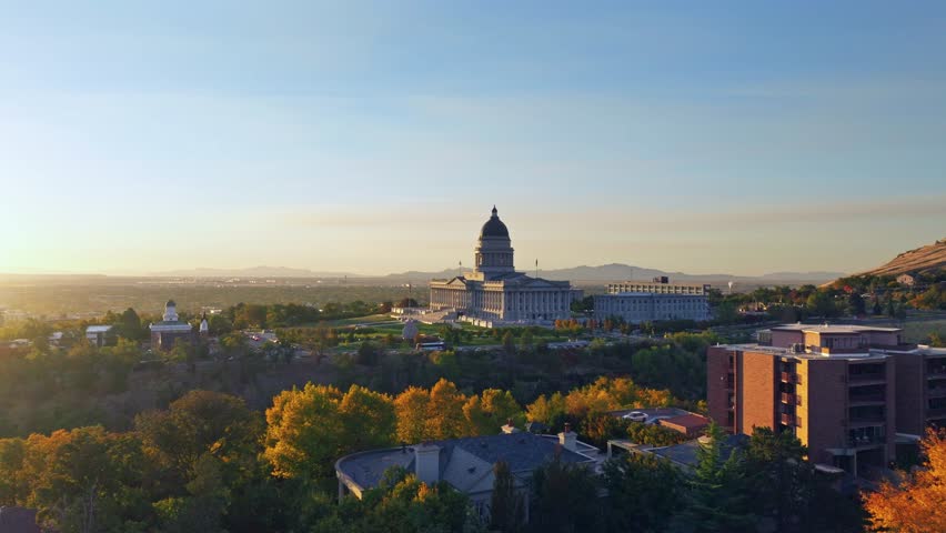 Utah State Capitol complex with beautiful green gardens illuminated by the setting sun in the fall. Low angle drone panning shot