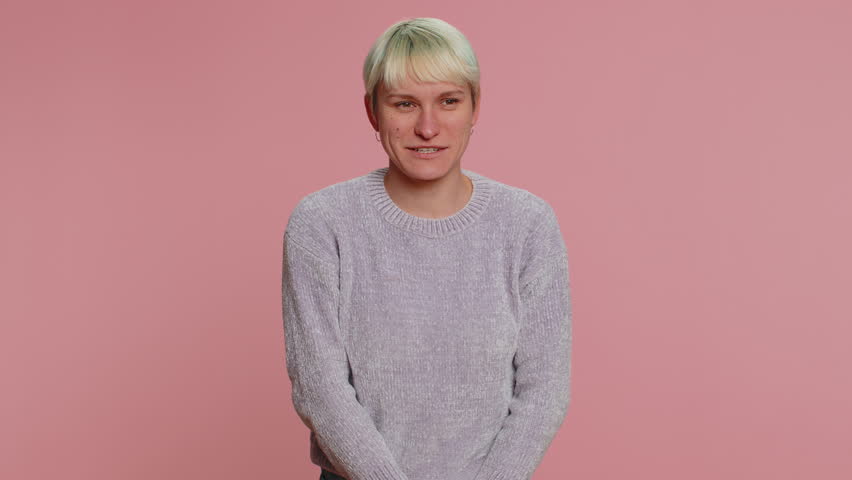 Woman with short hair pointing around with finger gun gesture, looking confident, making choice, shooting killing with hand pistol right on target. Girl on pink background. Lgbt gay lesbian people