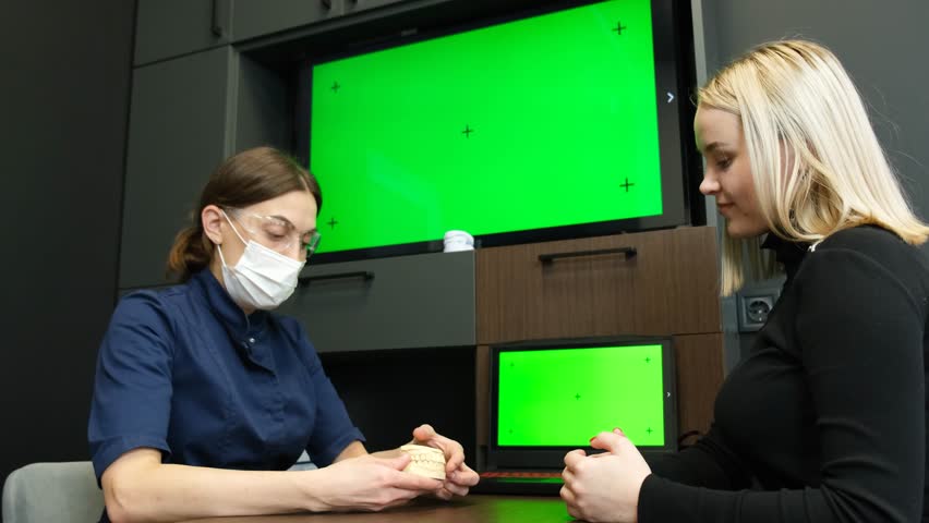 In a hospital, a female doctor shows a TV with a green Chroma Key screen to a patient. | Shutterstock HD Video #1099518941
