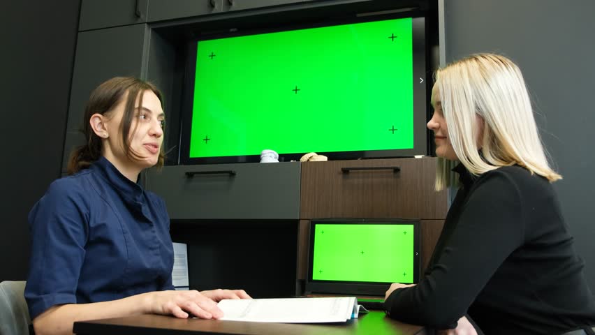 A doctor in a mask shows a laptop with a green screen to a patient | Shutterstock HD Video #1099518945