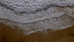 Bird's-eye view of an empty sandy beach. The waves are rolling on the shore. Slow Motion video drone shot