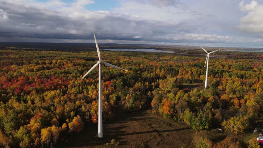 Couple of wind turbines surrounded by vibrant autumn forest, aerial orbit view