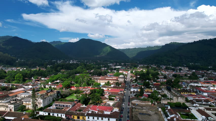 Aerial view of Antigua Guatemala by DJI air2s drone flying upwards above the city, revealing beautiful architecture and landscape of the city. Cloudy but sunny sky volcano, Fuego, in the background. | Shutterstock HD Video #1099524741