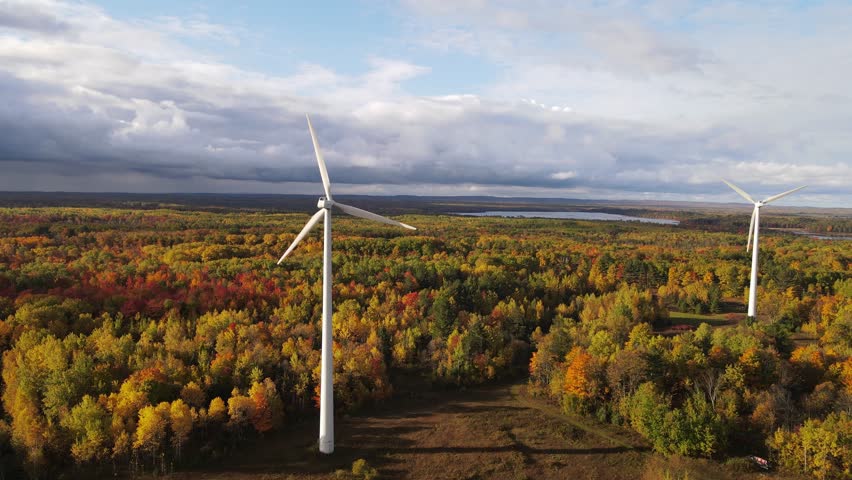Stormy clouds coming over wind turbines and autumn colored forest, aerial view
