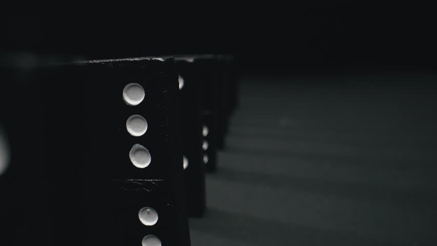 Domino effect. Close-up pushed dominoes falling in row. Concept of coherence and consequences of destabilization. Teamwork. A chain reaction on a dark surface with copy advertising space. Royalty-Free Stock Footage #1099526457