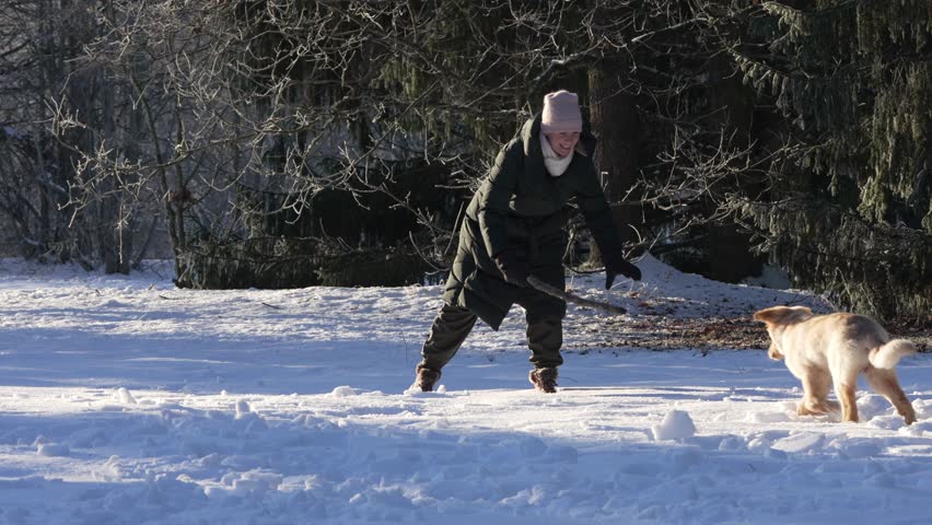 A young woman walking her dog snowy weather, outdoor. dog owner playing with puppy winter concept. playing with happy dog fun