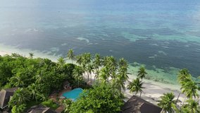 Aerial view of Indian Ocean in Balinese island with green palm trees near white sand beach and pool villas. Luxury living in villa by ocean. Top view of clean, deserted beach, palm trees and houses.