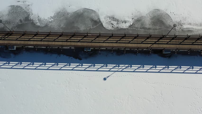 Wooden bridge construction on snowy frozen lake, aerial view