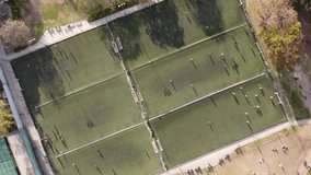 Aerial top-down rising directly above soccer players on row of football training fields 