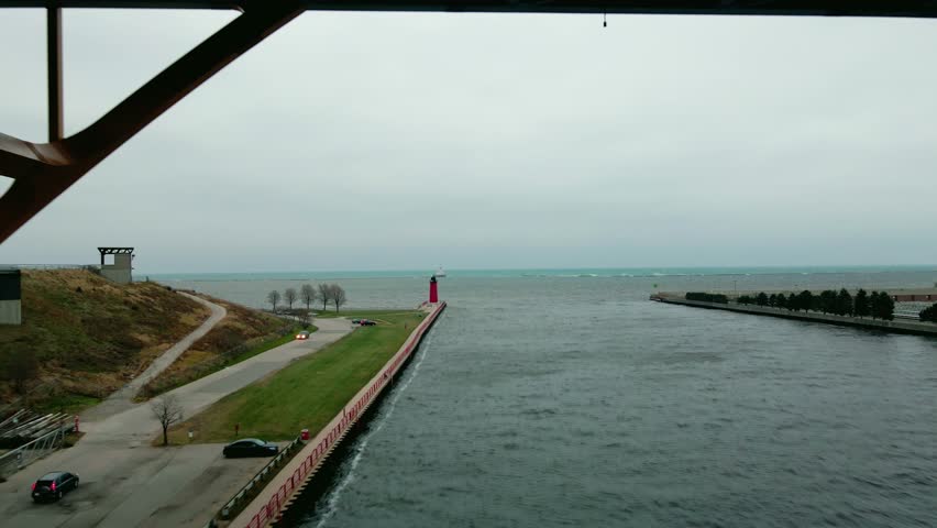Aerial shot over a river to a red lighthouse on a cloudy day, sea in the background. Milwaukee, Wisconsin, United States.
