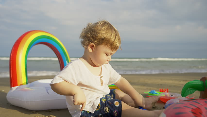 Caucasian family parents and baby boy enjoy and fun outdoor lifestyle travel the sea together on beach holiday vacation. Little child boy kid playing sand and beach toy at seaside at summer sunset. | Shutterstock HD Video #1099546863