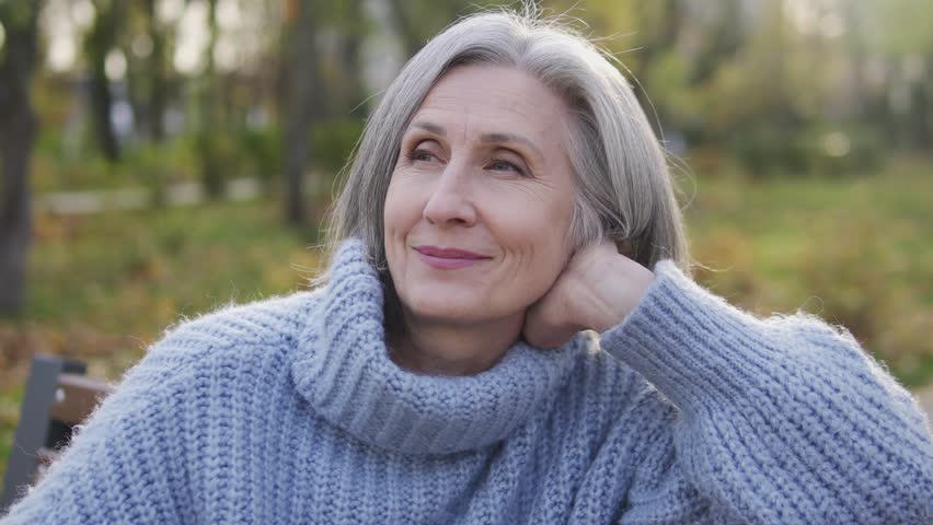 Happy inspired lady in her 60s sitting on bench in garden of her Vacation home, smiling and enjoying beautiful landscapes and fresh air, escape from bustled city, harmony | Shutterstock HD Video #1099549079