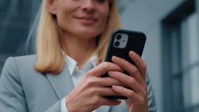 Close-up focus on mobile phone young caucasian woman holding smartphone standing outdoors sending electronic message email chatting on social media businesswoman communicates with client on internet