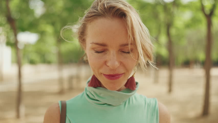 Close-up of an attractive happy woman with short blond hair wearing casual clothes, opens her eyes, smiles looking at the camera | Shutterstock HD Video #1099550947