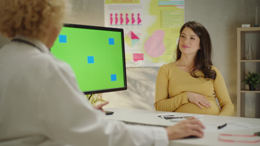 doctor shows a pregnant patient her unborn baby on an ultrasound screen. Female doctor typing keyboard. Green screen. Gynecology office