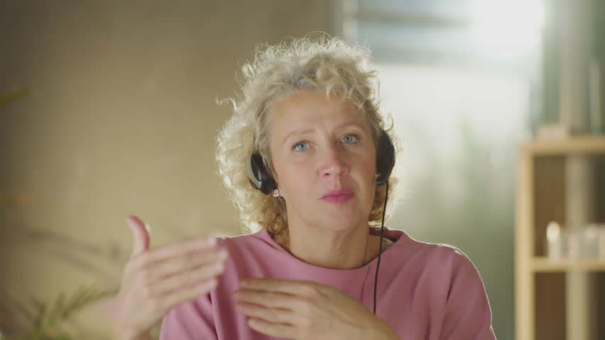 Mature businesswoman wearing headphones, looking at camera and communicating online with client | Shutterstock HD Video #1099551301