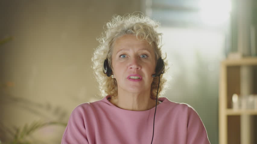 Mature businesswoman wearing headset talking to the camera in video conference chat. Female boss speaking during an online meeting | Shutterstock HD Video #1099551305