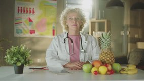 A female doctor sitting with different types of fruits on the desk whiling looking and smiling at camera - Powered by Shutterstock - Get 15% off with code: PIKWIZARD15