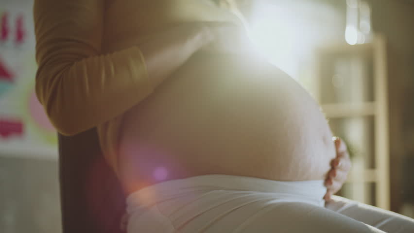 Close-up view of a young pregnant woman gently touching her belly in clinic | Shutterstock HD Video #1099551461