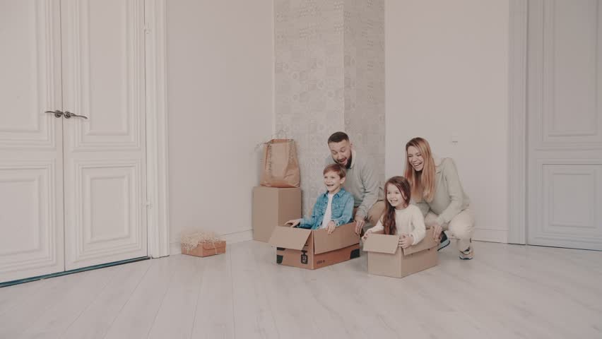 Funny active family playing on moving day, happy adult parents ,mom dad pushing cardboard boxes with cute little kids sit inside having fun packing relocate into new home concept, slow motion | Shutterstock HD Video #1099551881