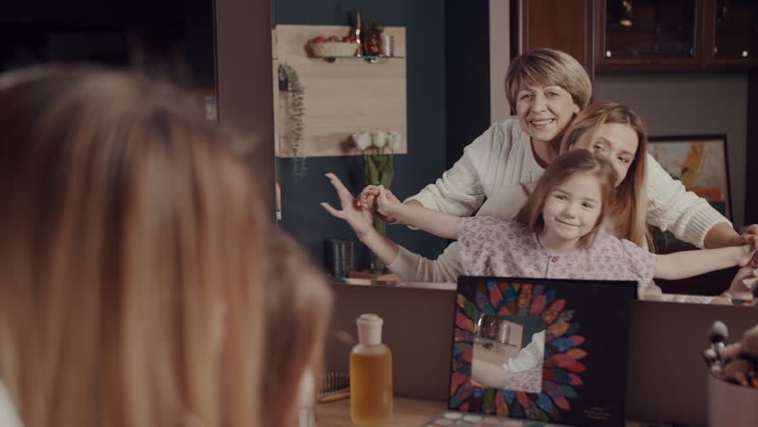 Three generations of women of a happy family, an old grandmother, a little daughter and a little girl have fun hugging, smiling, laughing in front of the mirror. Vivid emotions. One family story. | Shutterstock HD Video #1099551917