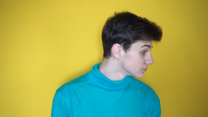 Young boy in blue shirt turns his head from side towards you and looking from under forehead with curious face, having suggestion. facial expression as I turn to you. Yellow horizontal background | Shutterstock HD Video #1099551959