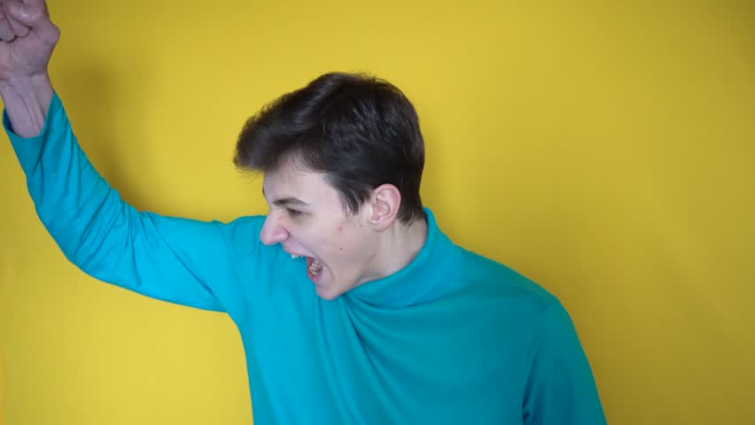 Acting classes, casting. Angry teenager in blue clothes points to the side with his hand and yells at someone and then laughing. Yellow horizontal background | Shutterstock HD Video #1099552167