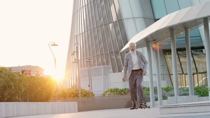 Active cool happy older senior business man skater wearing suit riding skateboard in city business office district after work on sunset. Old people freedom spirit concept. Slow motion. Royalty-Free Stock Footage #1099556497