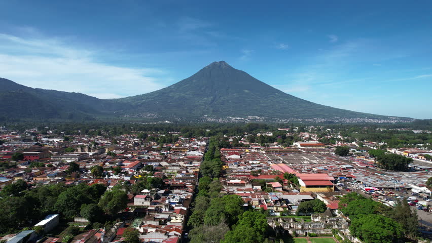Aerial view of Antigua Guatemala by DJI air2s drone flying latterly above the city, revealing beautiful architecture and landscape of the city. sunny sky volcano, Fuego, in the background. | Shutterstock HD Video #1099558143