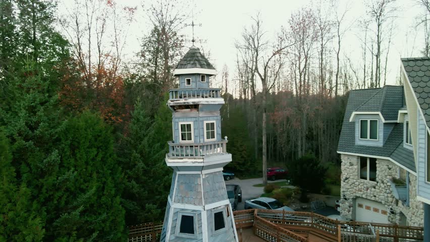 cinematic aerial orbiting around large blue mansion with a private lighthouse sorounded by green trees in Wisconsin, USA
