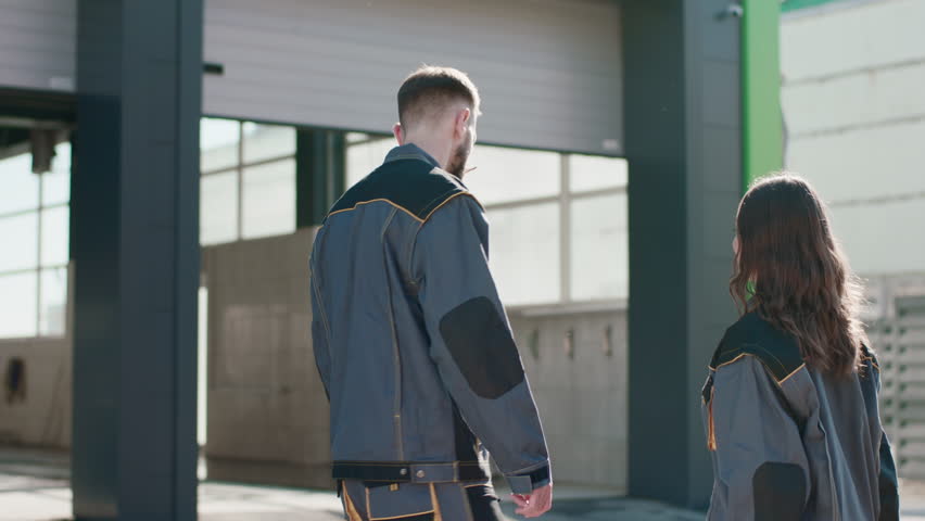 Two young people, a boy and a girl, dressed in overalls, shot from behind as they excitedly enter the car wash to start the work day. 4K.
