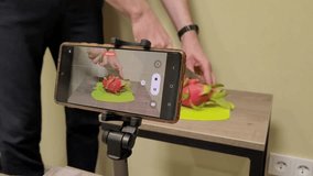 Shoot video on smartphone. Cut dragon fruit. Video for blog. Record cooking on video. The man cuts the fruit. Cutaway pitaya. Phone on a tripod.