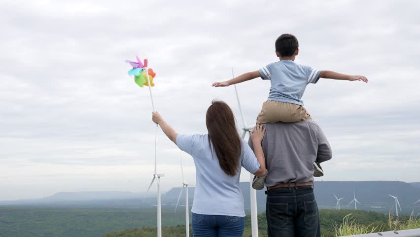 Concept of progressive happy family enjoying their time at the wind turbine farm. Electric generator from wind by wind turbine generator on the country side with hill and mountain on the horizon. | Shutterstock HD Video #1099560119
