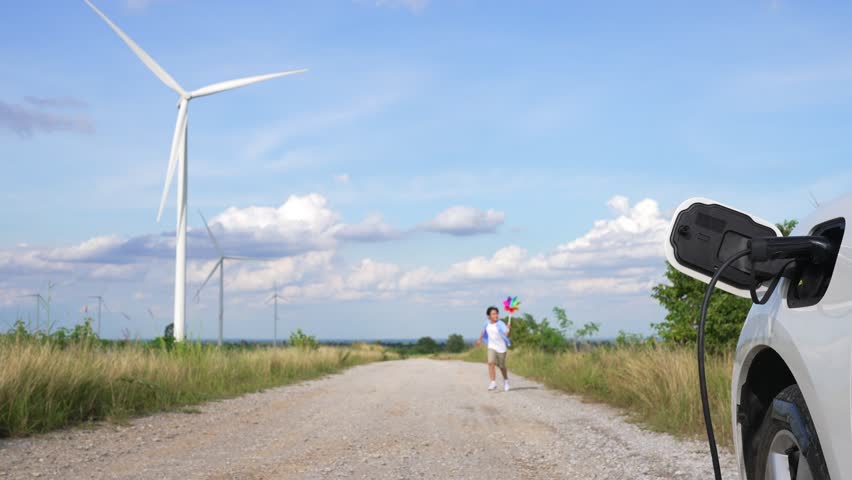 Progressive young boy playing windmill toy next to EV car at wind turbine farm. Electric generator from wind by wind turbine generator on the country side. | Shutterstock HD Video #1099560163