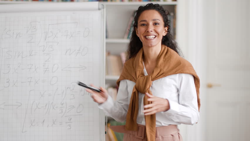 Math lecture. Close up portrait of young educated woman teacher explaining new topic to pupils online, standing near whiteboard with formulas and talking to camera, webcam pov Royalty-Free Stock Footage #1099560345