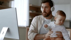 Remote work and parenthood. Young busy father businessman video chatting with partners via pc and carrying his active newborn baby on hands, working from home, tracking shot, free space