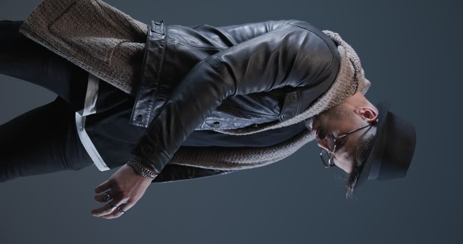 cool man with beard rubbing palms, looking to side, crossing arms and posing in the spotlight on grey background
