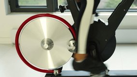 Closeup of spinning wheel on exercise bike at home on spin bicycle fitness workout. Woman training on stationary bike watching online video class for exercising cardio
