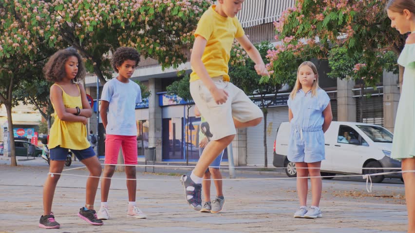 Group of kids playing with chinese jumping rope outdoors. Boys and girls having fun together. Royalty-Free Stock Footage #1099570553