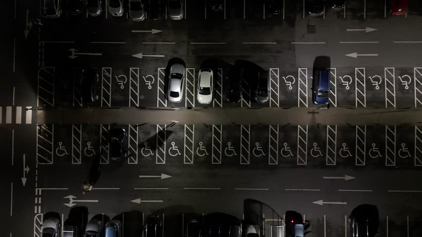 Aerial view of a supermarket car park at night with cars and people