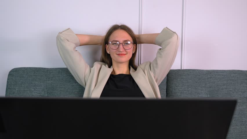 Smiling satisfied young businesswoman in glasses finished computer work stretching sitting at her desk with her hands behind her head. well done stress relief calm calm concept at work. | Shutterstock HD Video #1099580661