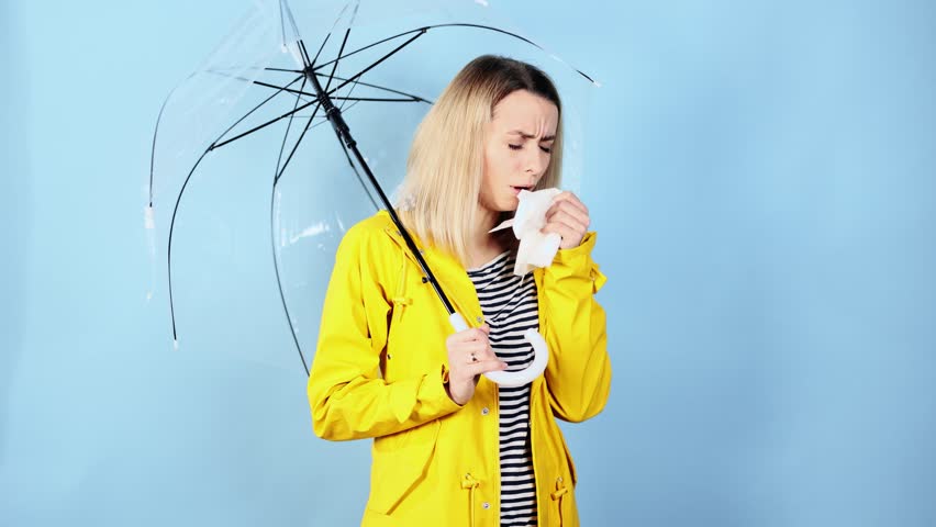 Sick young blond woman in yellow raincoat blowing running nose sneezing and coughing on isolated blue background Unhealthy female under umbrella getting flu virus symptom Cold and fever concept | Shutterstock HD Video #1099581471