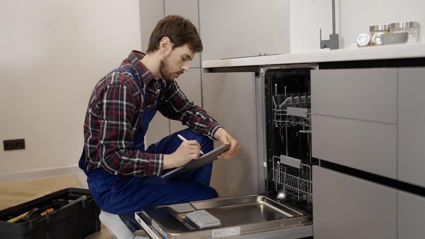 Repairman writing down list of spare parts for dishwasher repair, maintenance | Shutterstock HD Video #1099582797